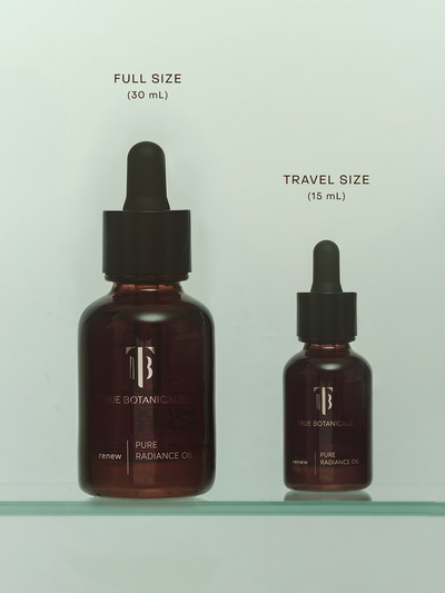 True Botanicals Renew Pure Radiance Oil shown in two sizes side by side on a glass shelf: the full size 30mL amber glass dropper bottle on the left and the travel size 15mL bottle on the right, both with black pipette tops and gold branding against a soft sage-green background.