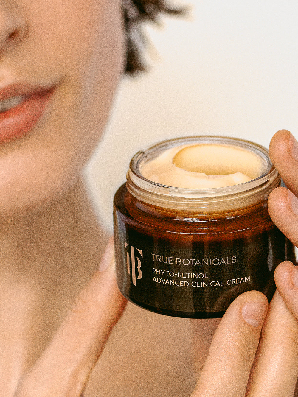 Woman holding a jar of True Botanicals phyto-retinol advanced clinical cream with a blurred background